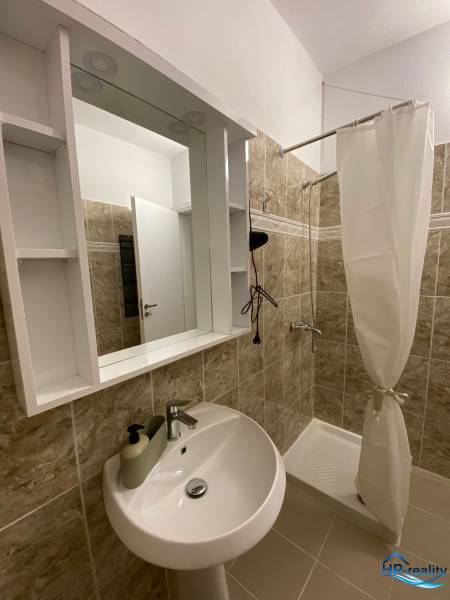Fürdőszoba a nyaraló apartmanban mosdóval, zuhanyzóval és polcokkal ellátott tükörrel.