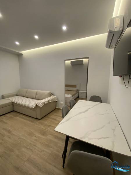 Nyaraló apartman nappalija kanapéval, étkezőasztallal és hálószobába vezető bejárattal.