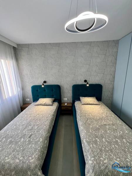 Kétszemélyes hálószoba geometrikus tapétával és modern világítással egy üdülő apartmanban.