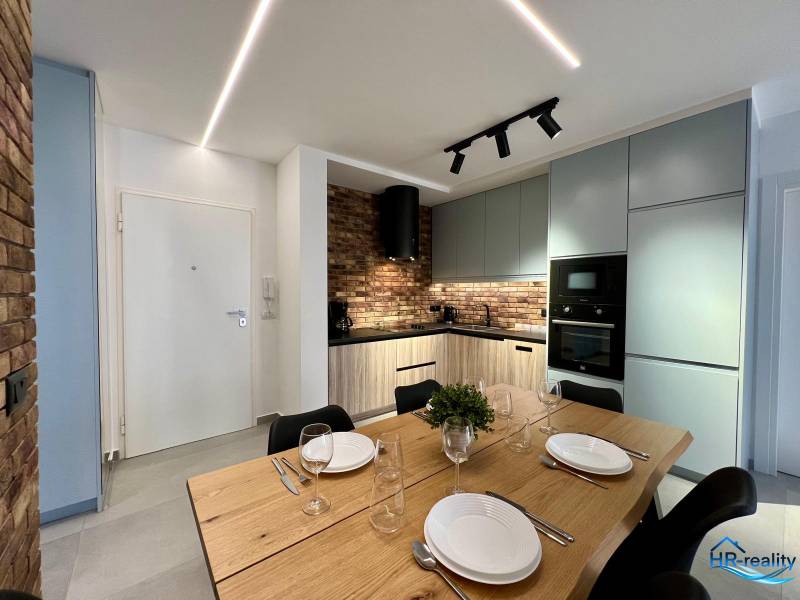 Konyha a nyaraló apartmanban étkezőasztallal, téglaburkolattal és modern készülékekkel.