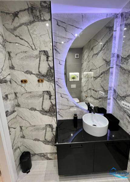 Fürdőszoba a nyaraló apartmanban kerek tükörrel és elegáns csempékkel.