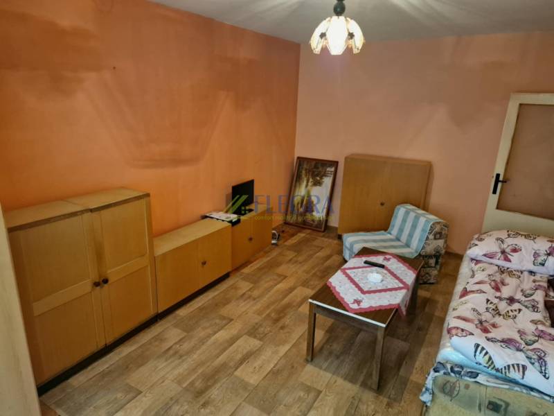 Szoba fából készült bútorokkal és egy fotellel egy egyszobás lakásban.