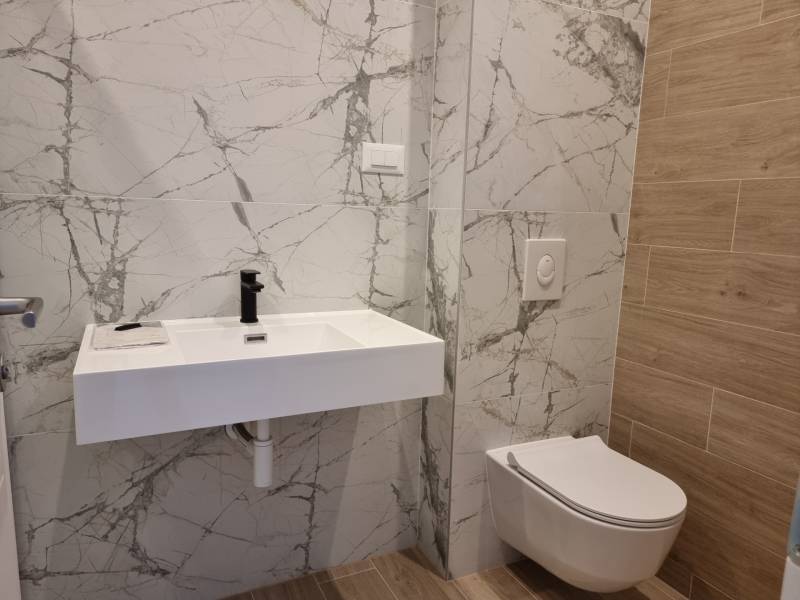 Fürdőszoba függesztett WC-vel, kerámia mosdóval és márvány csempékkel egy 4 szobás lakásban.