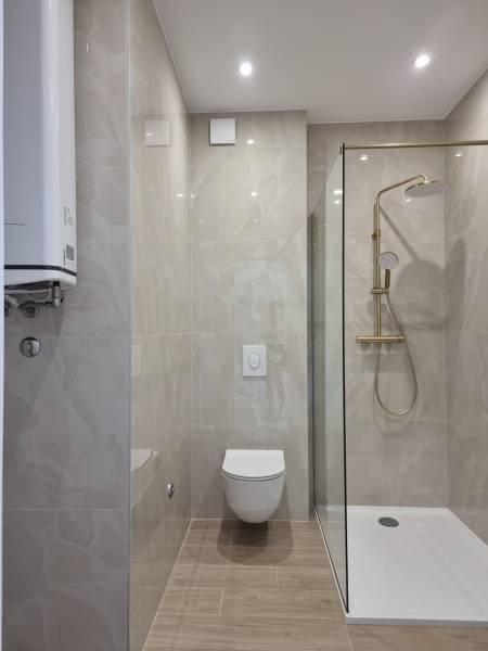 Fürdőszoba egy 4 szobás lakásban WC-vel, zuhanyzóval és sima csempékkel.