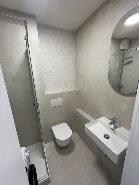Fürdőszoba garzonlakásban WC-vel, mosdóval és zuhanyzóval, finom árnyalatokban.