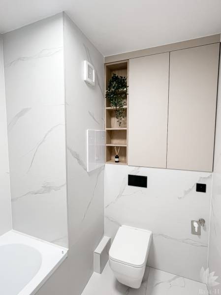 Minimalista fürdőszoba egy kétszobás lakásban WC-vel, káddal és tárolóhelyekkel.
