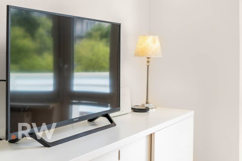 Televízió és lámpa a fehér komódon egy kétszobás lakásban.