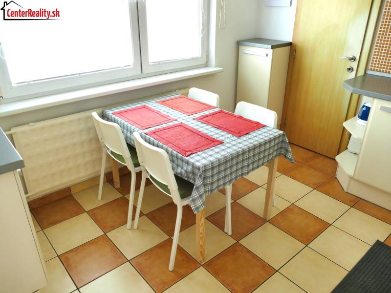 Ebédlő faasztallal és négy székkel egy háromszobás lakásban, kockás padlóval.
