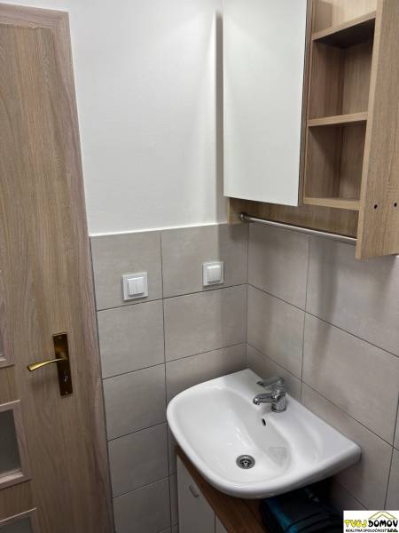 Fürdőszoba egy háromszobás lakásban mosdóval, tükörrel és faajtóval.