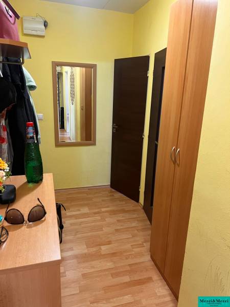 Folyosó egy háromszobás lakásban fa padlóval, beépített szekrénnyel és tükörrel.