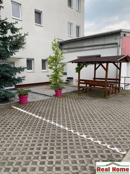 Kastély burkolattal, fa ülőhelyekkel és növényekkel rózsaszín virágtartókban a Šamorínska utcán.