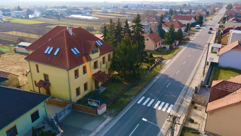 Egy épület a Chrabrany utcában, Topoľčanyban, házakkal és fákkal körülvéve, a főút mellett.