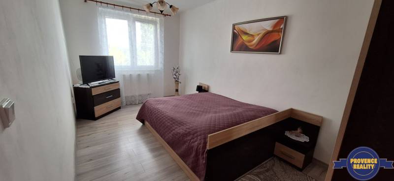 Hálószoba egy háromszobás lakásban ággyal, televízióval és faldekorációval.