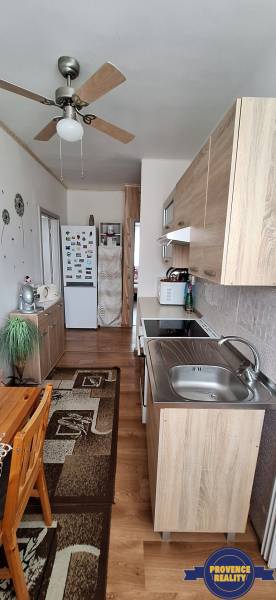 Konyha egy háromszobás lakásban fa bútorokkal és mennyezeti ventilátorral.