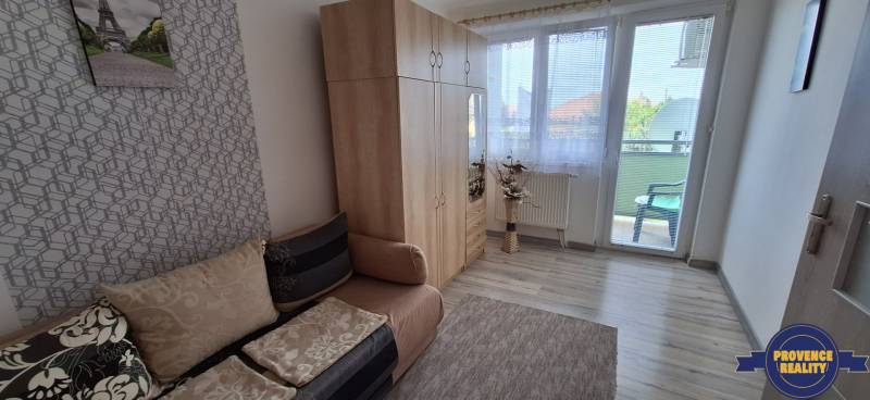 Szoba egy háromszobás lakásban kanapéval, gardróbbal és erkéllyel.