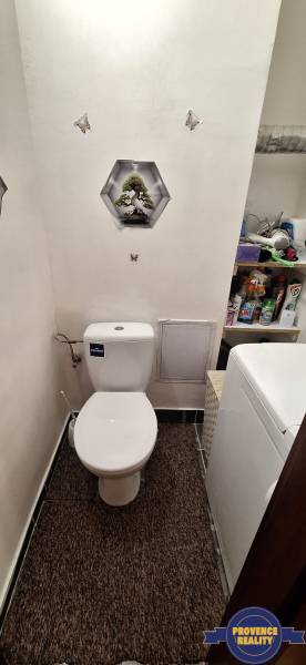 Fürdőszoba egy háromszobás lakásban WC-vel, mosógéppel és tisztítószerekkel teli polcokkal.