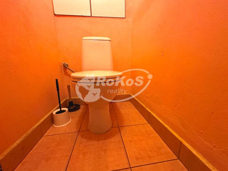 Narancssárga WC egy háromszobás lakásban, a WC-kefe a helyiség sarkában.