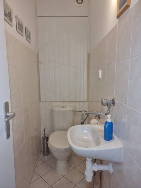 Kis fürdőszoba egy négy szobás lakásban WC-vel, mosdóval és világos csempével.