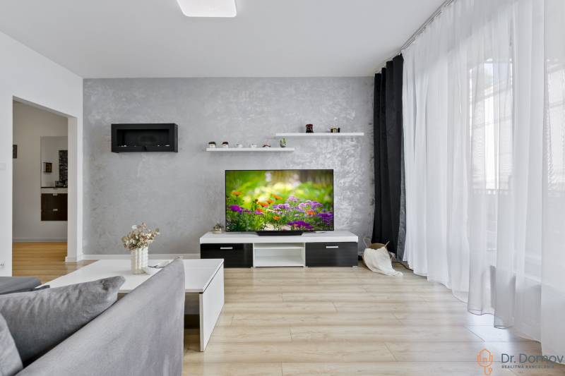 Nappali egy kétszobás lakásban televízióval, szürke fallal és fa padlóval.