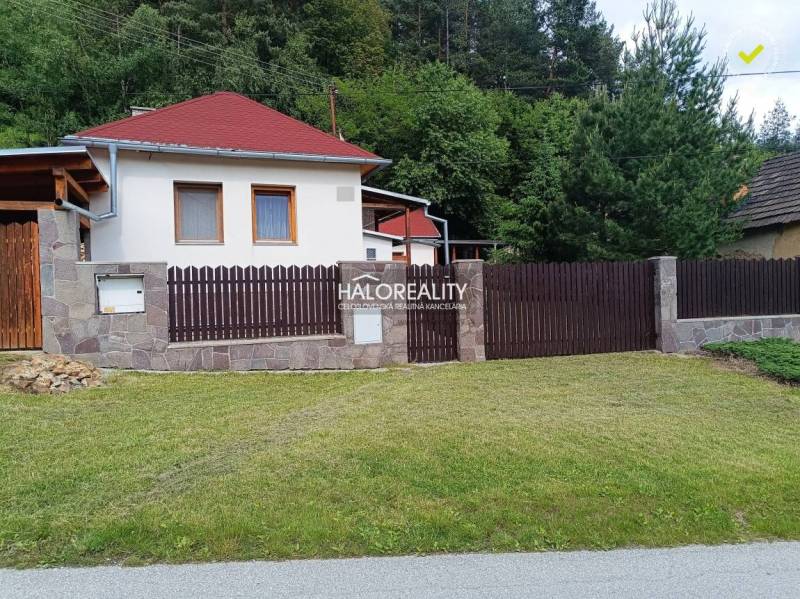 Egy helcmanovcei ház fa kerítéssel és rendezett gyepfelülettel, zöld növényzettel körülvéve.