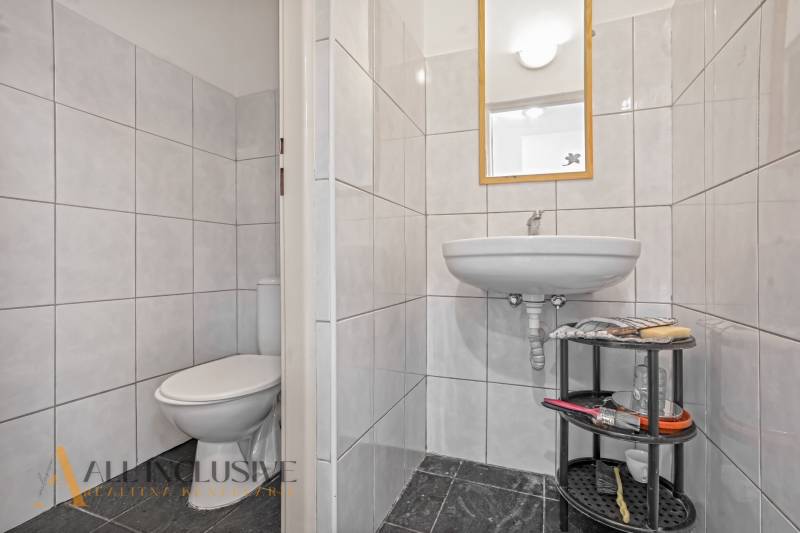 Fürdőszoba üzlethelyiségben mosdóval, WC-vel és kiegészítőknek szánt polccal.