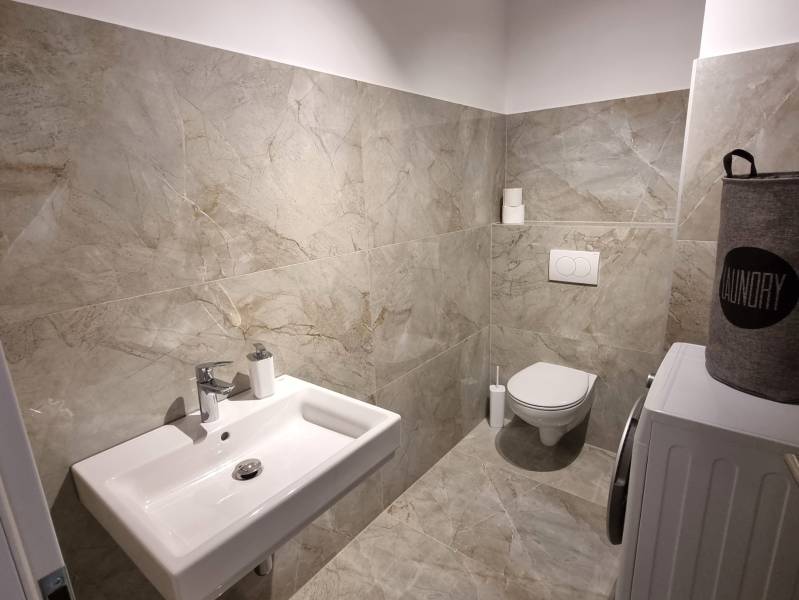 Fürdőszoba egy háromszobás lakásban mosdóval, WC-vel és mosógéppel, csempével burkolva.