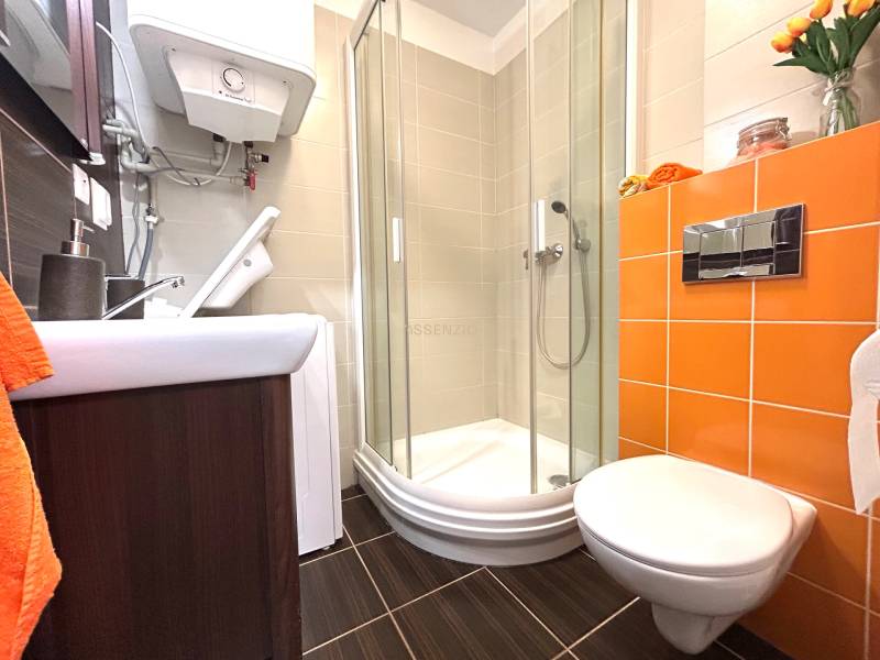Fürdőszoba a garzonlakásban WC-vel, zuhanyzóval és narancssárga csempékkel.