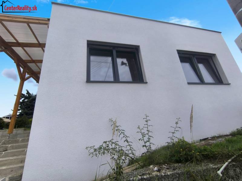 Családi ház Kis Kršteňanyban két nagy ablakkal és fa előtetővel.