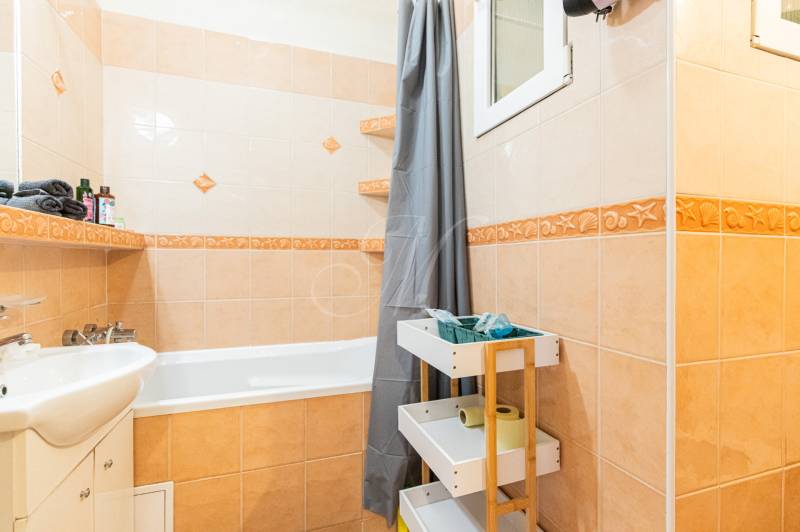 Fürdőszoba káddal, mosdóval és tárolóhellyel egy kétszobás lakásban.