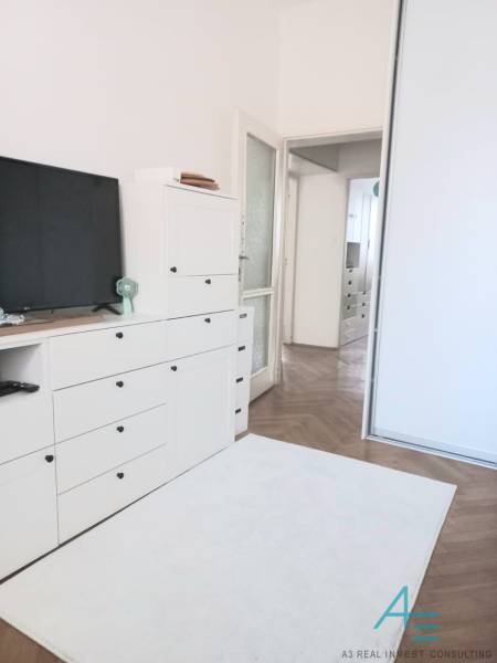 Fehér nappali egy 4 szobás lakásban, TV-vel, szekrényekkel és fa padlóval.