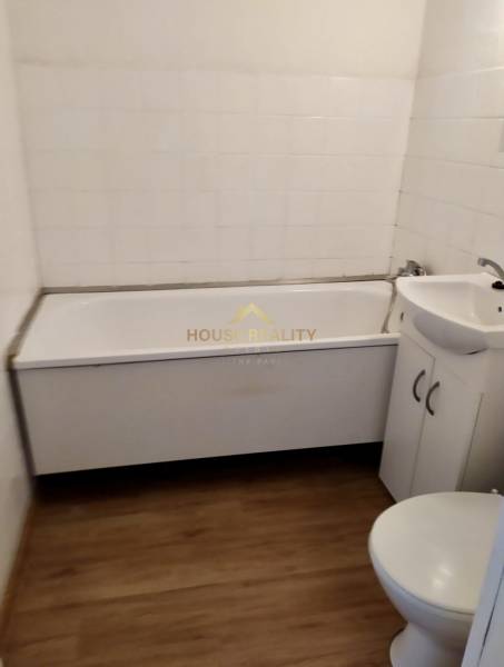 Fürdőszoba egy egyszobás lakásban káddal, mosdóval és WC-vel, fa hatású csempével.