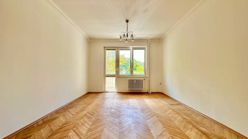 Tágas szoba egy háromszobás lakásban parkettás padlóval és nagy ablakokkal a fény számára.
