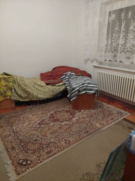 Szoba családi házban ággyal, szőnyeggel és csipkefüggönyökkel.