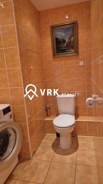 Fürdőszoba egy kétszobás lakásban mosógéppel, WC-vel és képpel a falon.