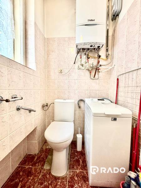Fürdőszoba egy kétszobás lakásban WC-vel, mosógéppel és falra szerelt gázkazánnal.