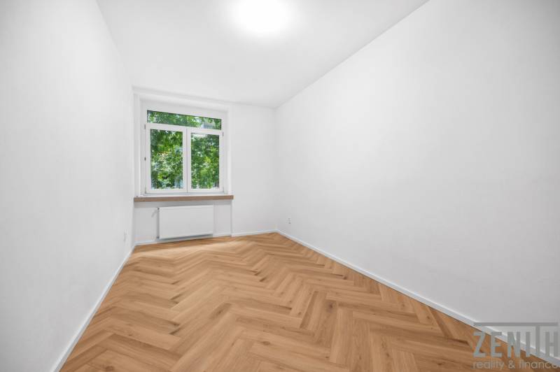 Szoba egy háromszobás lakásban parkettás padlóval és nagy ablakkal, világos dekorációval.