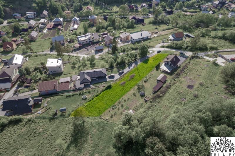 Légi felvétel Raková község lakóterületeiről, zöld domboldalak és házak.