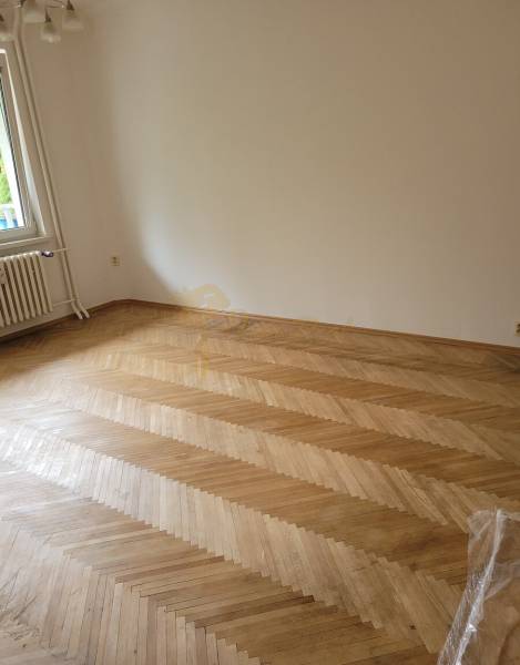 Üres szoba egy háromszobás lakásban parkettás padlóval és ablakkal.
