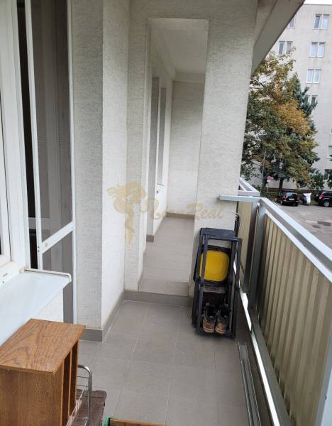 Erkély egy háromszobás lakásban összecsukható székekkel és kilátással az udvar fáira.