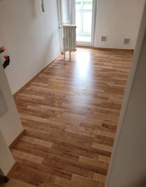 Egy háromszobás lakásban látható egy szoba fa padlóval és radiátorral.