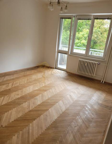 Szoba egy háromszobás lakásban fa padlóval és erkélyajtókkal.