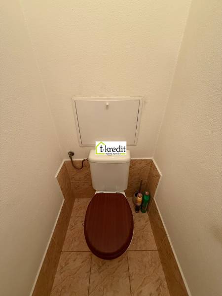 WC barna ülőkével és csempékkel egy kétszobás lakásban.