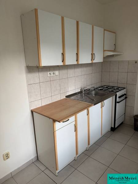 Konyha gáztűzhellyel, fehér szekrényekkel és mosogatóval egy kétszobás lakásban.