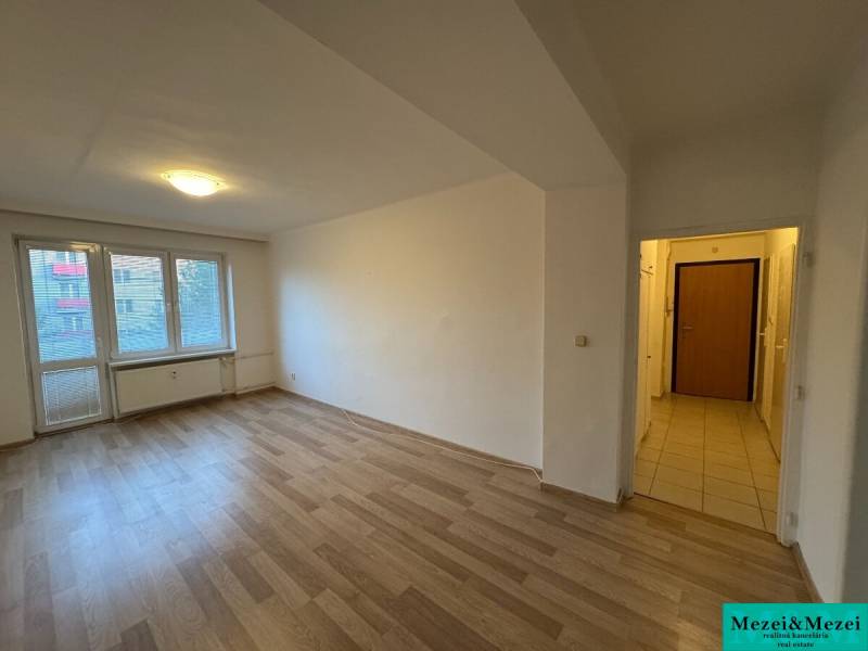 Tágas szoba laminált padlóval egy 2 szobás lakásban, napfény árad be a nagy ablakon keresztül.