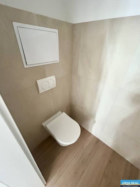 WC rejtett öblítéssel egy 3 szobás lakásban, világos csempékkel és fa padlóval körülvéve.