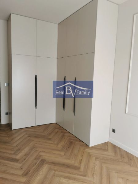 Fehér sarokszekrény és fa dekorációjú padló egy kétszobás lakásban.