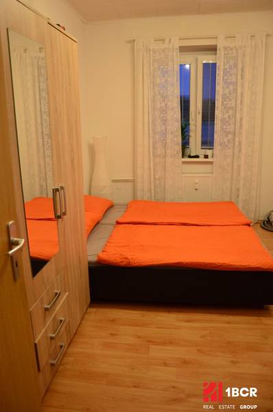 Hálószoba egy kétszobás lakásban ággyal, szekrénnyel és fa dekorációjú padlóval.