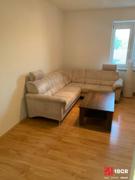 Nappali egy kétszobás lakásban sarokkanapéval és fa mintázatú padlóval.