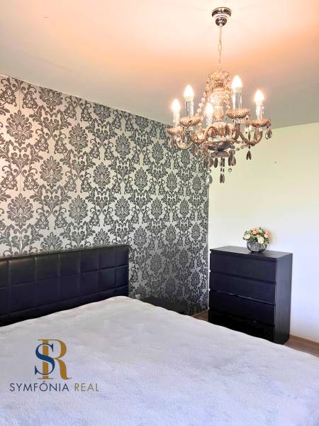 Hálószoba csillárral és tapétás fallal egy családi házban. Fa dekoros padló.