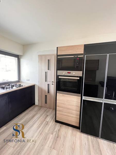 Konyha családi házban gáz tűzhellyel és háztartási gépekkel, fa mintázatú padlóval.